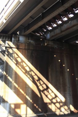 Paslı metal köprü kirişleri altında geometrik gölgeler bırakan güneş ışığı
