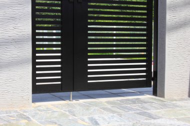 Modern siyah metal kapı, dışarıda çizgili gölgeler bırakıyor.