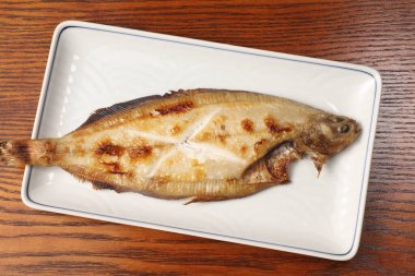 Tüm balığı ızgara beyaz seramik tabakta dinleniyor.