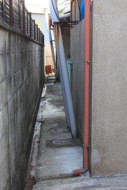 Borularla yan yana uzanan yüksek binalar arasındaki dar beton sokak.
