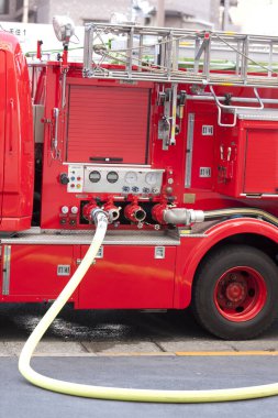Kırmızı itfaiye aracı sarı hortumla caddenin yanına park etmiş.