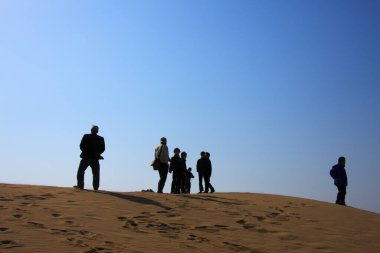 İnsanlar çölde kumulda mavi gökyüzüne karşı duruyorlar.