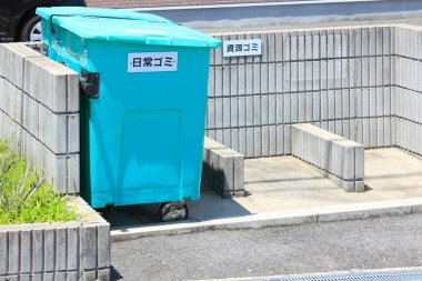 Betonun içinde duran büyük turkuaz çöp konteynırları.