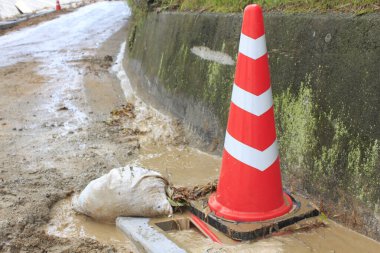 Turuncu trafik konisi ıslak çamurlu yol kenarının yanında duruyor