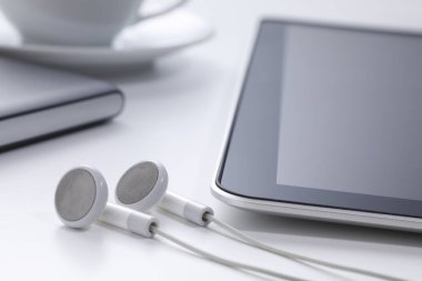 tablet bilgisayar ve kulaklıklar, arka planda kahve fincanı.     