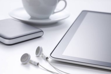 tablet bilgisayar ve kulaklıklar, arka planda kahve fincanı.     