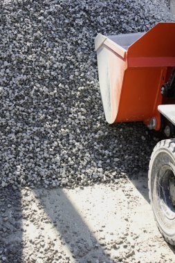 Turuncu inşaat aracı dışarıdaki büyük yığına çakıl döküyor.