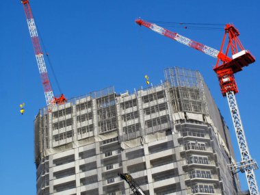 İnşaat vinçlerinin düşük açılı görüntüsü ve mavi gökyüzüne karşı yeni konut binaları     