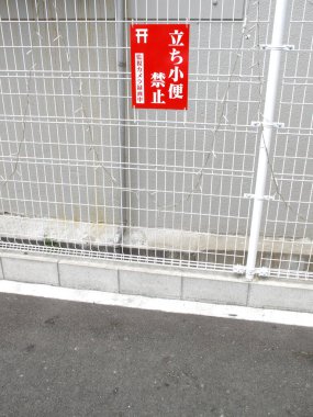 Beton duvarın yanındaki beyaz metal çitte kırmızı Japon işareti var.