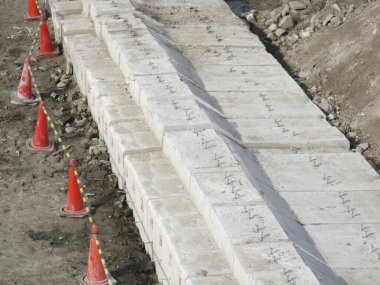 Toprak inşaat alanının yanında büyük beton bloklar bariyer oluşturuyor.