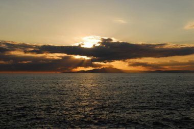 Manzaralı tepelerle deniz kıyısında güzel bir gün batımı.     