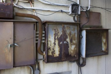 Paslı metal elektrik kutuları yıpranmış beton duvara monte edilmiş.