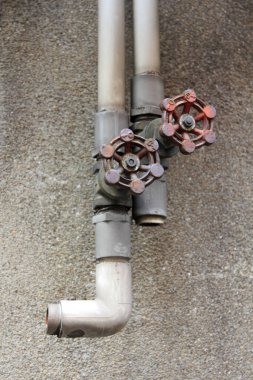 Duvardaki paslı metal borular iki kırmızı vanayla birleşiyor.