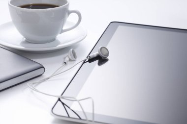 tablet bilgisayar ve kulaklıklar, arka planda kahve fincanı.     