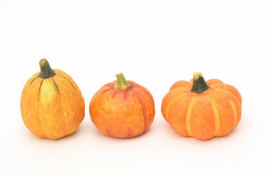 Beyaz bir yüzeyde üç minyatür balkabağı.