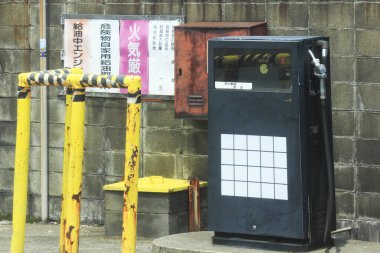 Sarı metal bariyerlerin yanında duran eski benzin pompası.