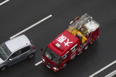 Kırmızı itfaiye aracı otoyolda gümüş arabanın yanından geçiyor.