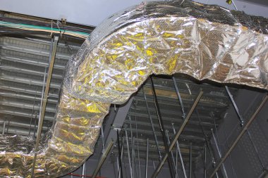 Tamamlanmamış endüstriyel tavan yapısı boyunca uzanan yalıtımlı hava kanalı