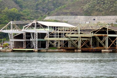 Bitmemiş metal yapı sakin nehir suyunun yanında duruyor.