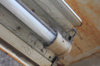 Yakın plan, kenarlarında örümcek ağları birikmiş tozlu floresan lamba armatürünü gösteriyor