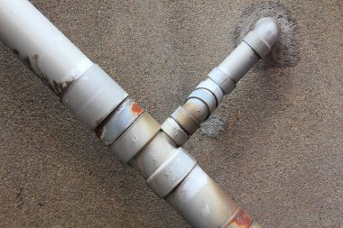 Paslı metal borular sert beton duvar yüzeyinde kesişiyor.