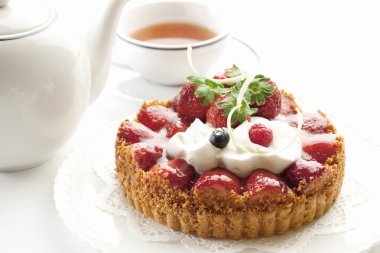 Çilekli lezzetli tart ve arka planda çay, yakın plan.