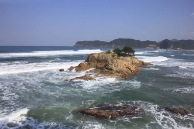 Ortasında küçük bir ada olan kayalık bir sahil.