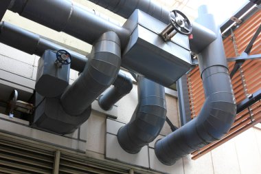 Dış duvar boyunca uzanan büyük endüstriyel havalandırma boruları.