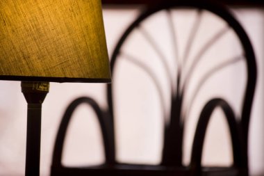 Arka planda pervane arkası bir koltuğun gölgesinde parlayan bir abajur..