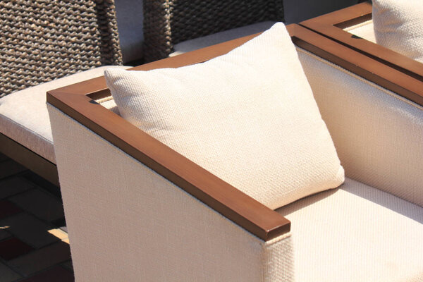 Sunlit outdoor armchair featuring beige cushion and wooden armrests