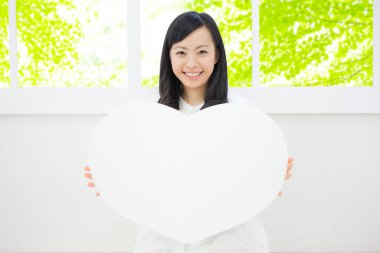 Beyaz bir kalp taşıyan ve kameraya gülümseyen güzel bir genç kadının portresi.