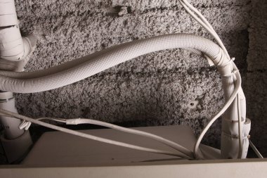 Yalıtımlı borular ve elektrik kabloları desenli beton duvar boyunca çalışıyor.