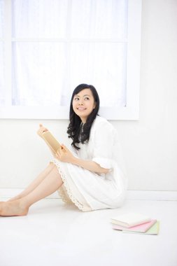 Asyalı kadın evde kitap okuyor. 