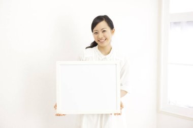 Güzel Asyalı genç bir kadının portresi açık renkli bir iç mekânda boş afiş taşıyor.