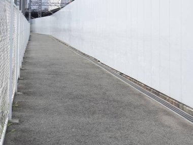 Metal çit ile beyaz duvar arasındaki beton yolu daralt