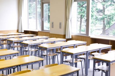 Okuldaki boş sınıfın içinde. Sıralar dolusu tahta masa ve sandalye.