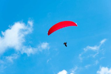 Mavi gökyüzünde kırmızı paraşüt üzerinde uçan paraglider