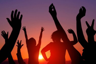 Mutlu insanların siluetleri gün batımında el kaldırdı.