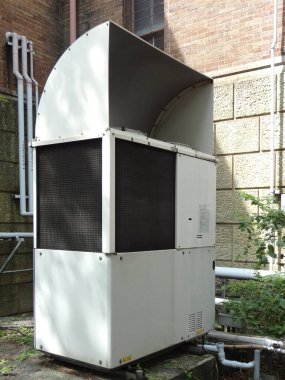 Tuğla bina duvarının yanında duran büyük endüstriyel klima ünitesi.