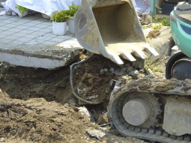 Kırık beton kaldırım ve açık arazinin yakınını kazan kazıcı.