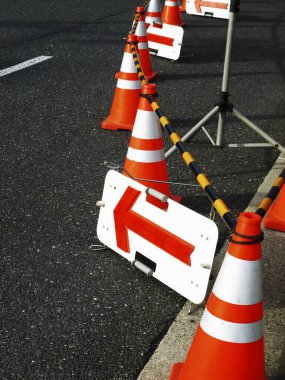 Turuncu trafik konileri ok işaretinin yanında asfalt yolu kaplıyor