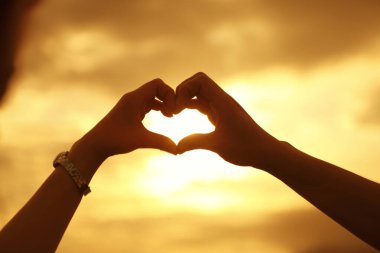 Altın günbatımı gökyüzüne karşı kalp şeklinde eller