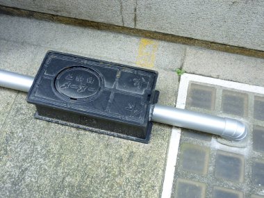 Kanalizasyon borusunun yakınındaki beton yüzeyde duran siyah ağırlık