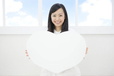 Beyaz bir kalp taşıyan ve kameraya gülümseyen güzel bir genç kadının portresi.