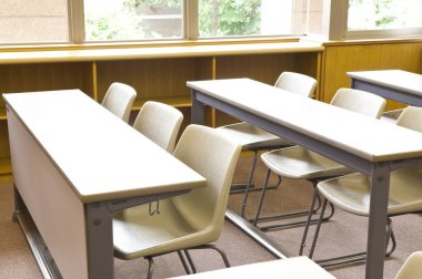 Okuldaki boş sınıfın içinde. Sıralar dolusu tahta masa ve sandalye.