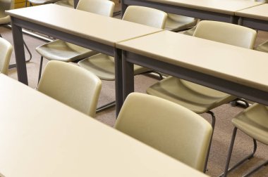 Okuldaki boş sınıfın içinde. Sıralar dolusu tahta masa ve sandalye.