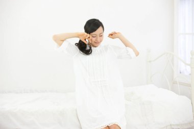 Beyaz yatak odasındaki güzel Asyalı genç kadın..