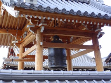 Geleneksel Japon ahşap yapısının içinde asılı büyük bronz çan.
