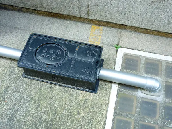 Kanalizasyon borusunun yakınındaki beton yüzeyde duran siyah ağırlık