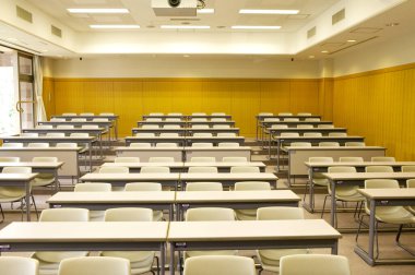 Okuldaki boş sınıfın içinde. Sıralar dolusu tahta masa ve sandalye.